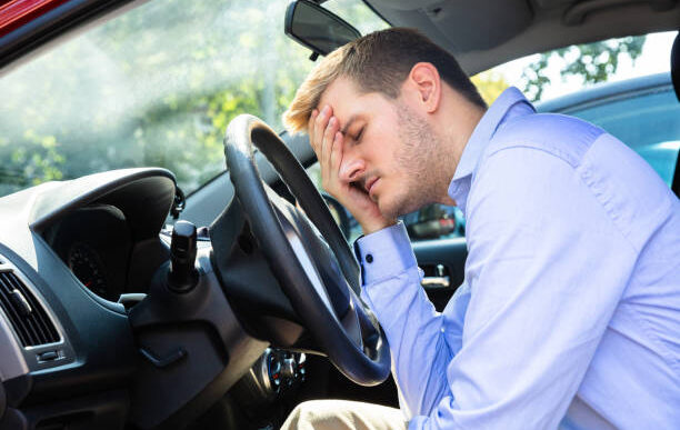 man leaning head on steering wheel inside car